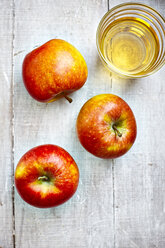 Three apples and a glass of apple juice on grey wood, elevated view - KSWF001249