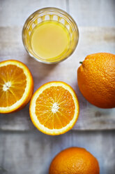 Oranges, halves of oranges and a glass of orange juice on grey wood, elevated view - KSWF001253