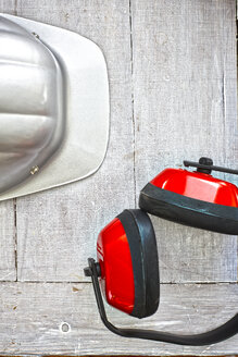 Safety helmet and red ear protection on grey wood, elevated view - KSWF001266