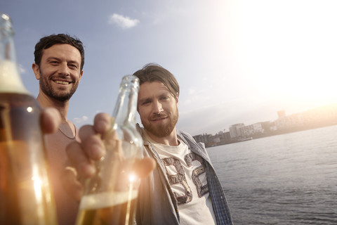 Porträt von zwei Freunden mit Bierflaschen am Flussufer, lizenzfreies Stockfoto