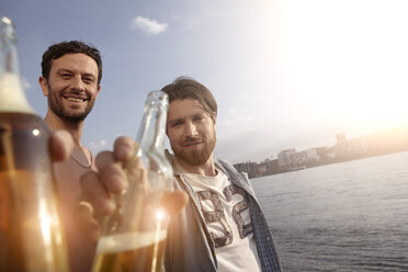 Portrait of two friends with beer bottles on riverbank - FMKF001183