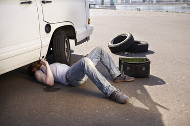 Man lying on ground repairing car - FMKF001203