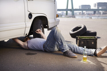 Man lying on ground repairing car - FMKF001204