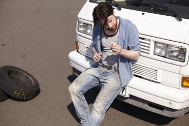 Man leaning against car looking at dipstick - FMKF001205