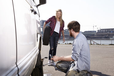 Smiling couple changing car tyre at minivan - FMKF001221