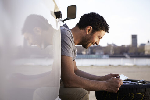 Mann sitzt im Auto und schaut auf ein digitales Tablet - FMKF001222