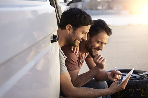 Zwei Männer sitzen im Auto und schauen auf ein digitales Tablet - FMKF001224