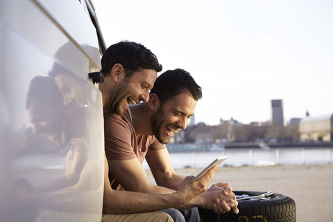 Zwei lachende Männer sitzen im Auto und schauen auf ein digitales Tablet, lizenzfreies Stockfoto