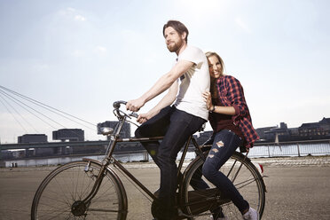 Happy couple riding bicycle on riverbank - FMKF001244