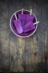 Plate of four yoghurt blueberry ice lollies on wooden table, elevated view - LVF001128