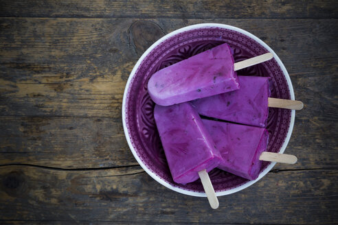 Plate of four yoghurt blueberry ice lollies on wooden table, elevated view - LVF001129