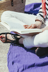 Spanien, Barcelona, Junge Frau sitzt an der Wand und liest ein Buch - EBSF000232