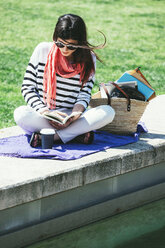 Spain, Barcelona, Young woman sitting on wall reading book - EBSF000233