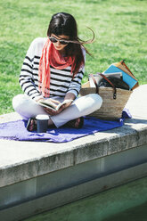 Spanien, Barcelona, Junge Frau sitzt an der Wand und liest ein Buch - EBSF000233