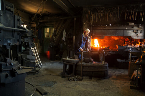 Germany, Bavaria, Josefsthal, senior blacksmith at work in historic blacksmith's shop - TCF003959