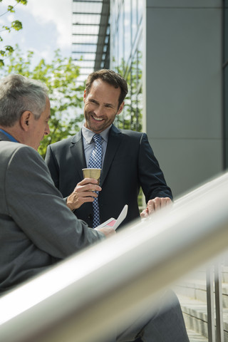 Zwei Geschäftsleute besprechen Dokumente vor einem Bürogebäude, lizenzfreies Stockfoto