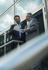 Two businessmen discussing documents outside office building - UUF000423