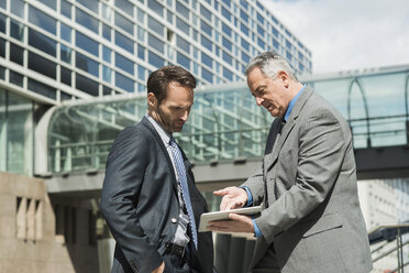 Two businessmen with digital tablet outside office building - UUF000453