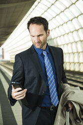 Geschäftsmann am Bahnhof schaut auf sein Handy - UUF000366