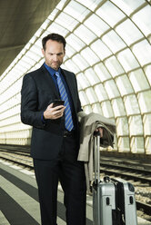 Businessman at train station looking at cell phone - UUF000367