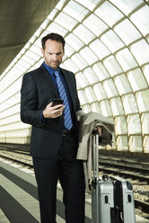 Geschäftsmann am Bahnhof schaut auf sein Handy - UUF000367