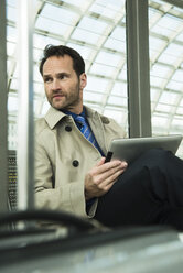 Businessman at train station using digital tablet - UUF000378