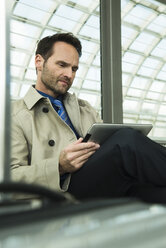 Businessman at train station using digital tablet - UUF000379