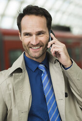 Lächelnder Geschäftsmann am Bahnhof beim Telefonieren - UUF000380