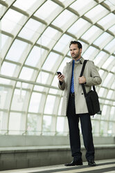 Businessman at train station holding cell phone - UUF000386