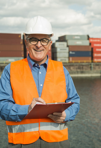 Mann mit Klemmbrett und Warnweste im Containerhafen, lizenzfreies Stockfoto