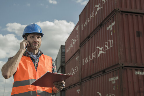 Mann mit Klemmbrett beim Telefonieren im Containerhafen - UUF000421