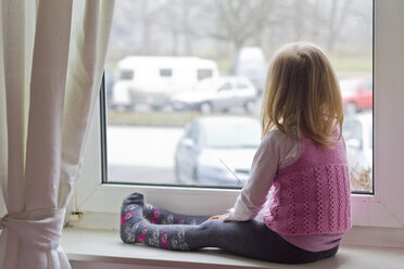 Little girl sitting on window sill looking out of window - JFEF000403