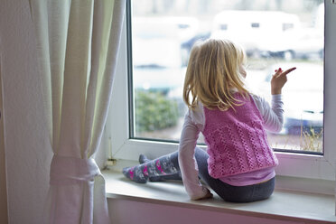 Little girl sitting on window sill looking out of window - JFEF000404