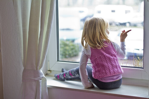 Kleines Mädchen sitzt auf der Fensterbank und schaut aus dem Fenster - JFEF000404