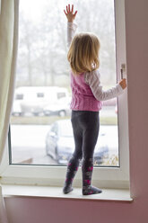 Little girl standing on window sill looking out of window - JFEF000405