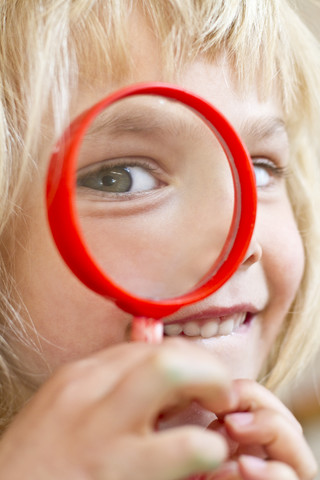 Porträt eines kleinen Mädchens, das durch ein Vergrößerungsglas schaut, lizenzfreies Stockfoto