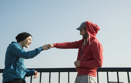 Junger Mann und Teenager am Geländer unter blauem Himmel - UUF000404