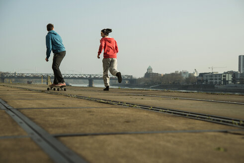 Junger Mann und Teenager beim Joggen und Skateboardfahren - UUF000446