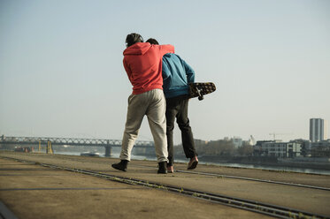 Young man and teenager with skateboard hugging - UUF000449