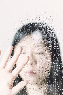 Asiatische Frau mit geschlossenen Augen hinter einer Fensterscheibe mit Wassertropfen - FLF000424