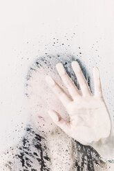 Asiatische Frau hinter dem Fenster drückt mit der Hand gegen die Scheibe mit Wassertropfen - FLF000425