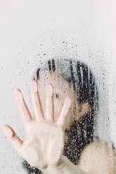 Asiatische Frau hinter dem Fenster drückt mit der Hand gegen die Scheibe mit Wassertropfen - FLF000427