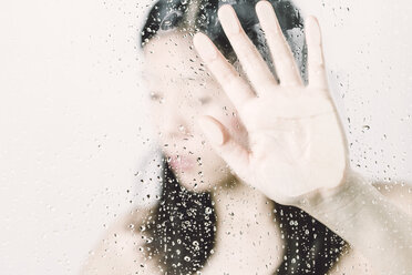 Asian woman behind window pressing hand against pane with water drops - FLF000428