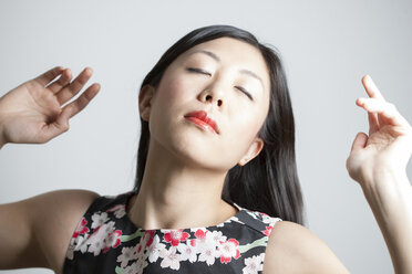 Porträt einer asiatischen Frau mit geschlossenen Augen vor einem grauen Hintergrund - FLF000504