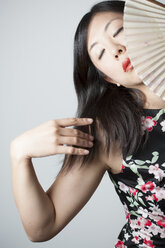 Portrait of Asian woman with closed eyes holding fan in front of grey background - FLF000505