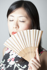 Porträt einer asiatischen Frau mit geschlossenen Augen, die einen Fächer vor einem grauen Hintergrund hält - FLF000507