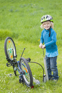 Little boy inflating bicycle tire on a meadow - MJF001082