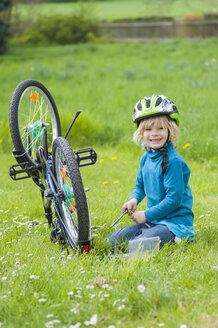 Porträt eines lächelnden kleinen Jungen, der auf einer Wiese ein Fahrrad repariert - MJF001083