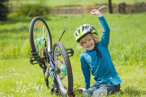 Porträt eines lächelnden kleinen Jungen, der auf einer Wiese ein Fahrrad repariert - MJF001090