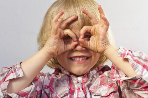 Porträt eines kleinen Mädchens, das mit den Fingern eine Brille formt, lizenzfreies Stockfoto